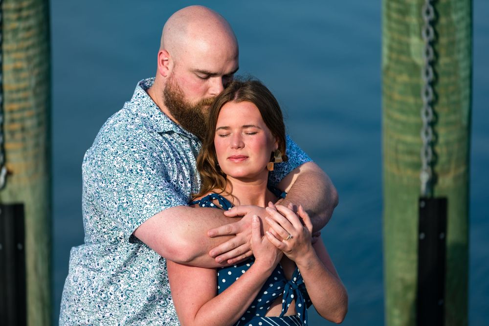 A couple embraces outdoors against turquoise green pillars during a tender moment at sunset.