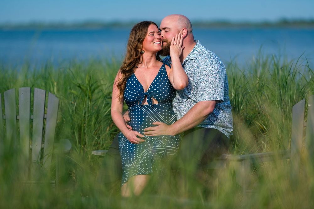 A romantic couple embraces in tall grass by the water on a bright summer day.