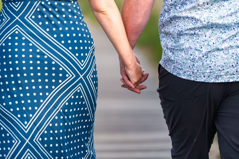 Person wearing a blue and white polka dot dress holds hands with someone in a gray patterned shirt and black pants.