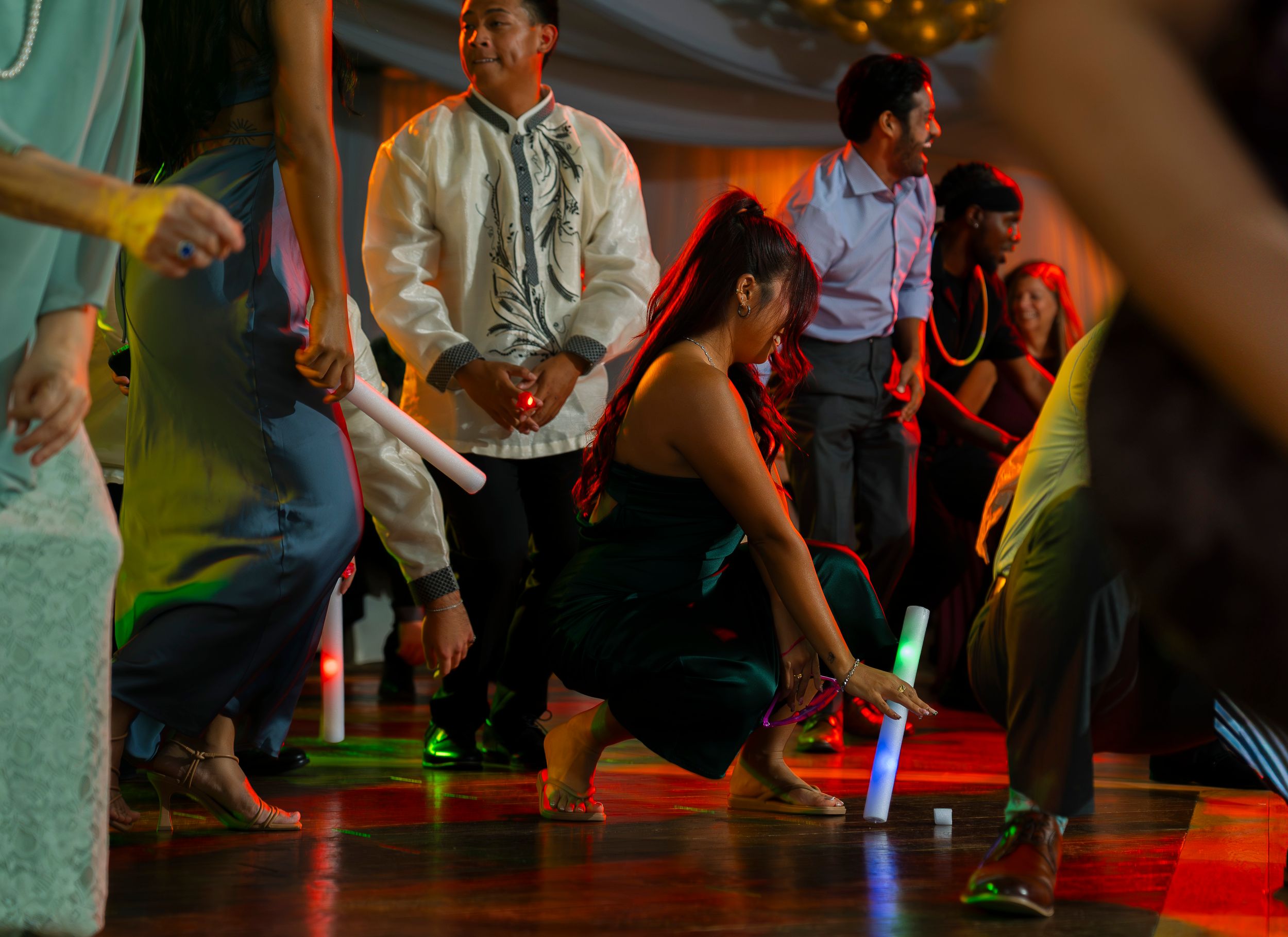 Party guests dancing and playing with light-up toys on a dimly lit dance floor.