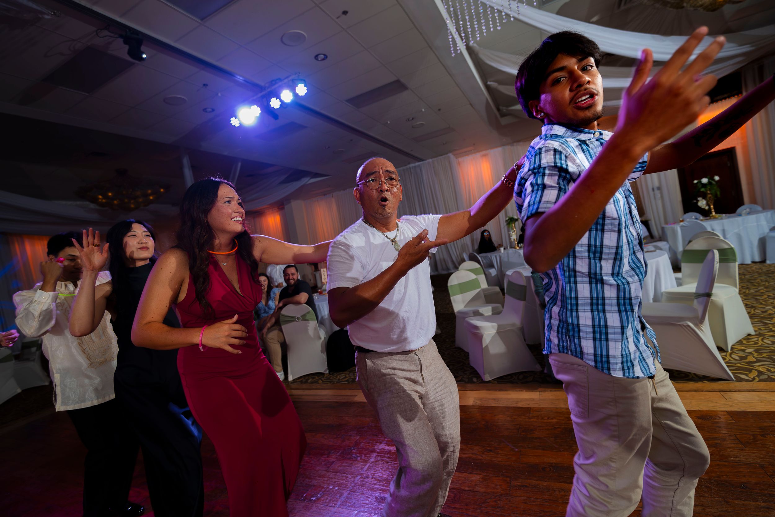 A group of people dancing energetically at an indoor event with blue stage lights in the background.