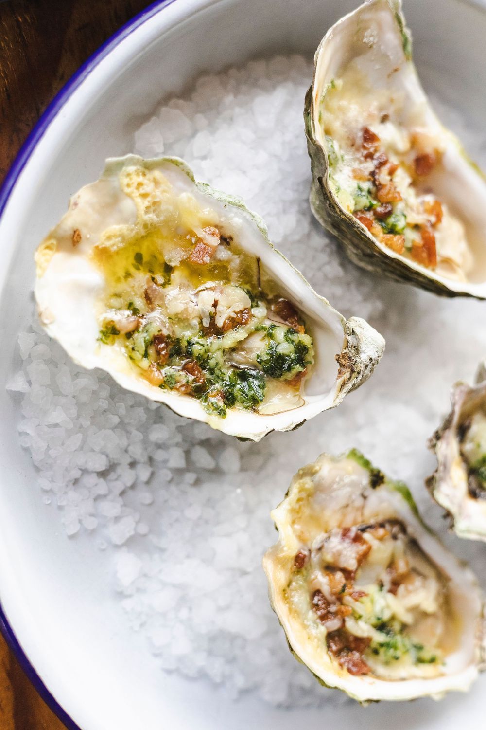 Fresh oysters garnished with herbs and seasonings served on a bed of crushed ice on white plates.