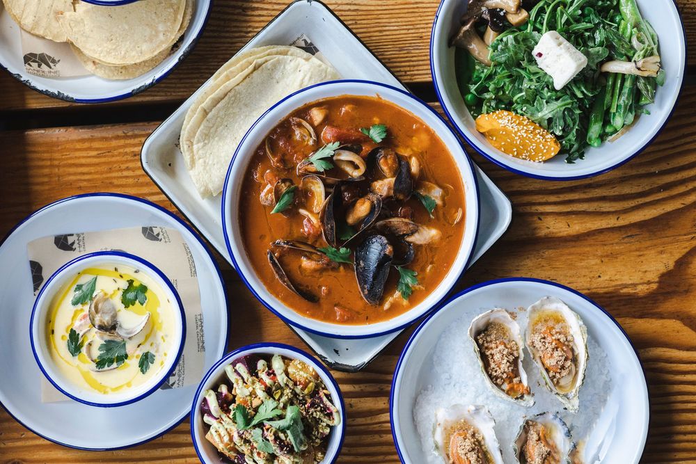 Rustic wooden table set with various bowls of Asian soups, noodles, and side dishes with blue-rimmed plates.