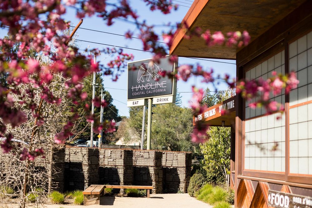 Pink cherry blossoms frame a rustic stone and wood building entrance with a business sign in spring.