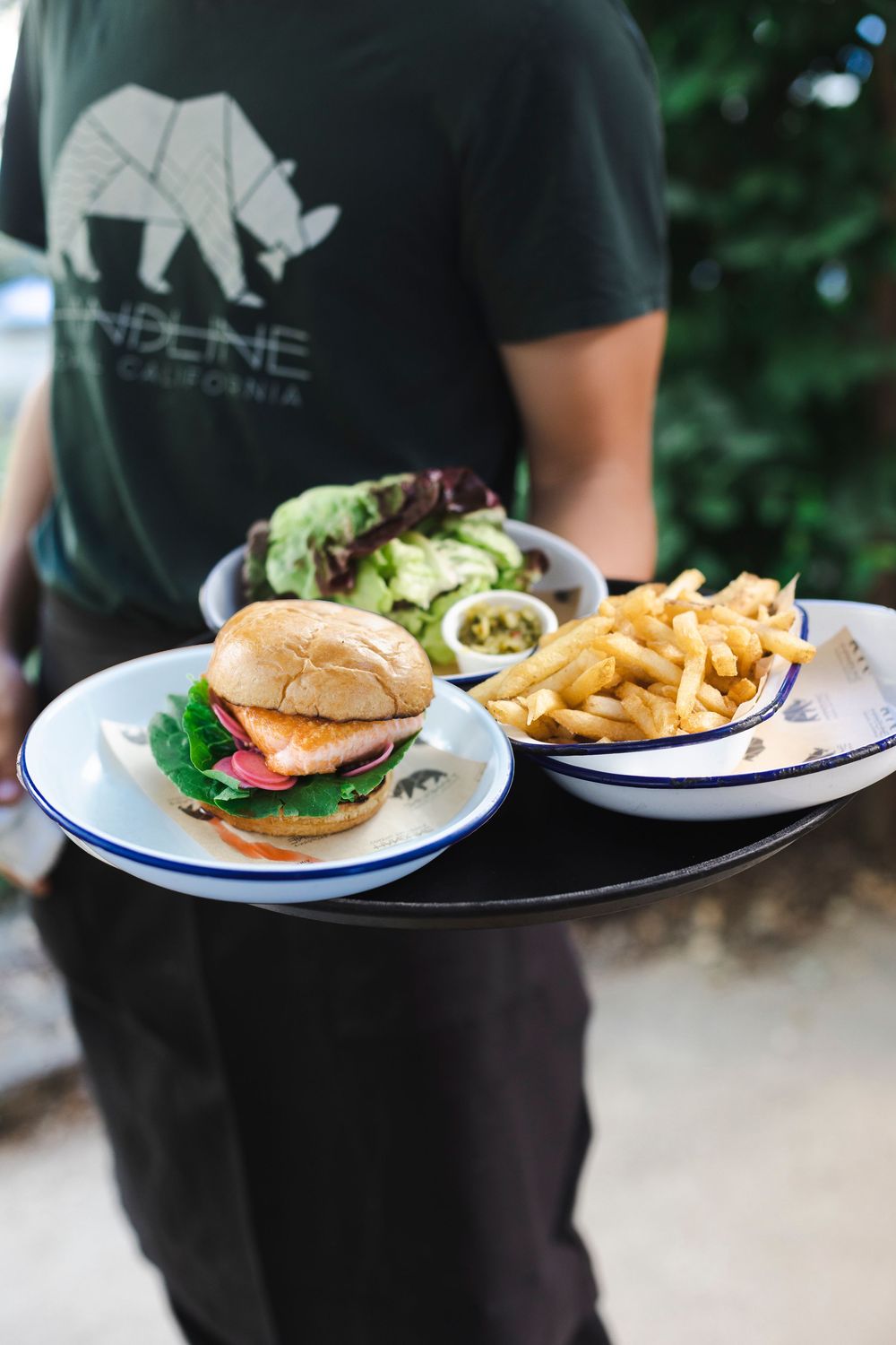 Hamburger plates with french fries served on white plates with blue rims in a casual restaurant setting.