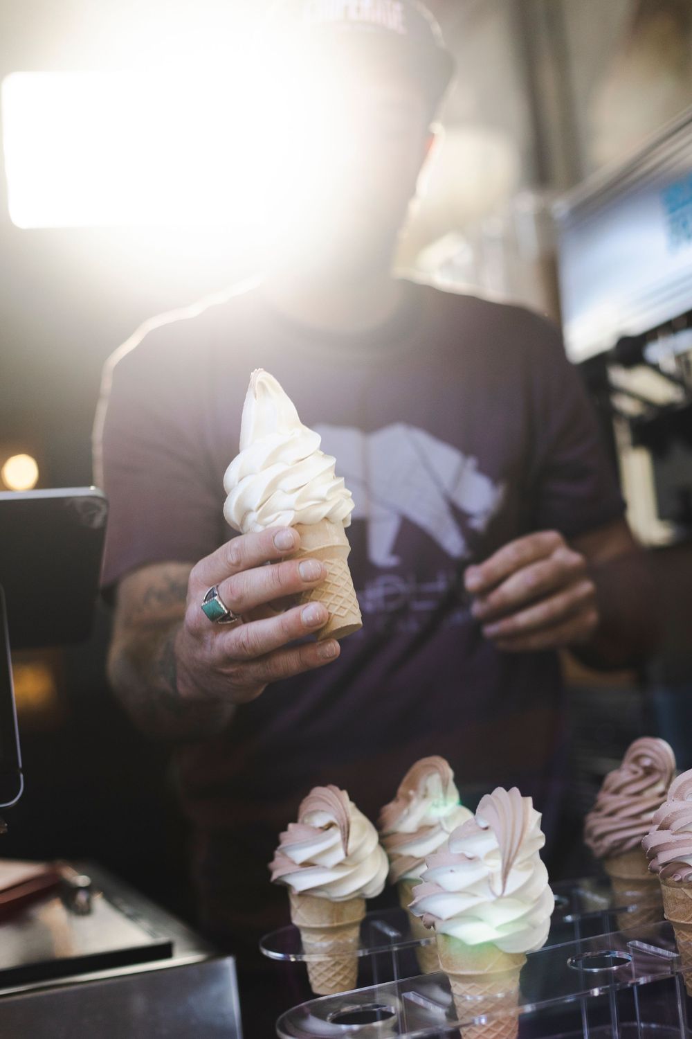 A sequence of hands holding soft serve ice cream cones in a dimly lit setting.
