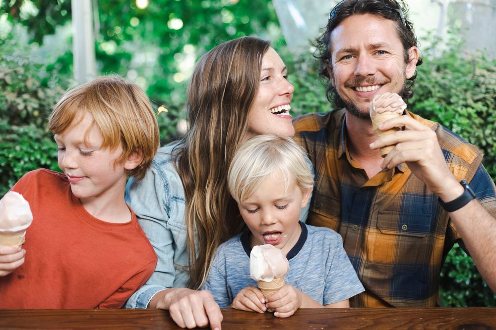 A happy family enjoying ice cream together outdoors on a sunny day with greenery in the background.