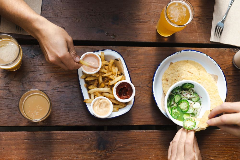 Multiple hands reach for drinks and appetizers on a rustic wooden table during a social gathering.