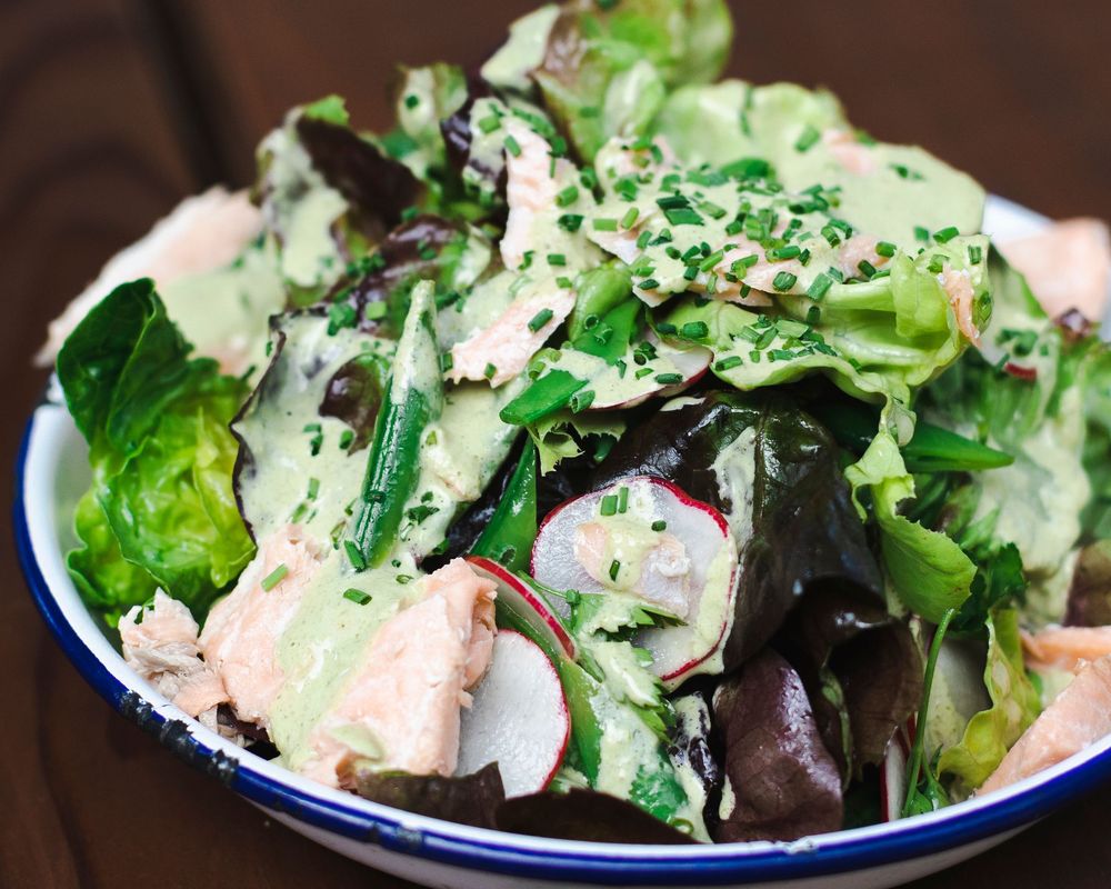 Fresh mixed green salad with black sesame seeds and creamy dressing served in a blue-rimmed bowl.