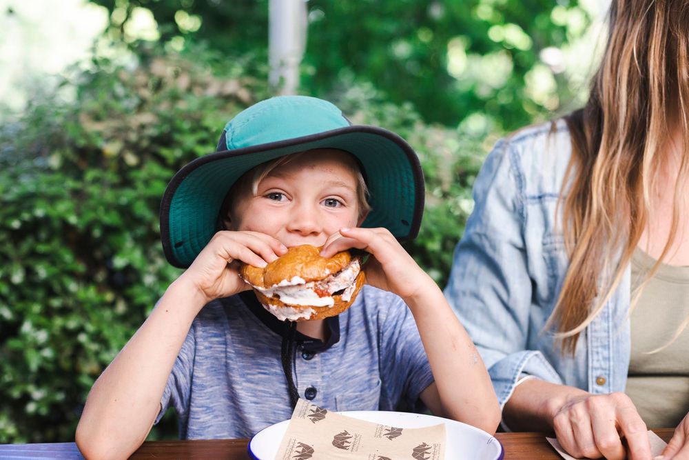 People enjoying delicious hamburgers while sitting at an outdoor picnic table in a lush garden setting.