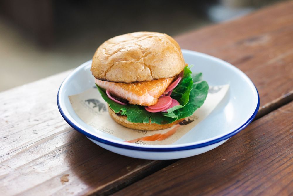 A row of classic hamburgers on white plates with blue rims arranged on a rustic wooden table surface.
