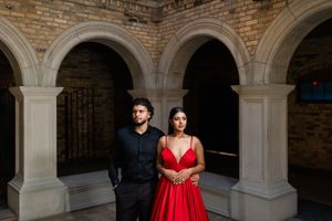 Couple in formal attire poses in archway corridor with brick walls and elegant stone columns.