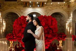 Romantic couple dancing in an elegant ballroom decorated with dramatic red roses and crystal chandeliers.