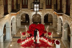 Elegant wedding ceremony setup in historic church with dramatic red rose petal aisle and white columns.
