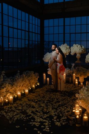 Romantic candlelit scene with glowing lanterns illuminating white floral arrangements in a dark indoor space.