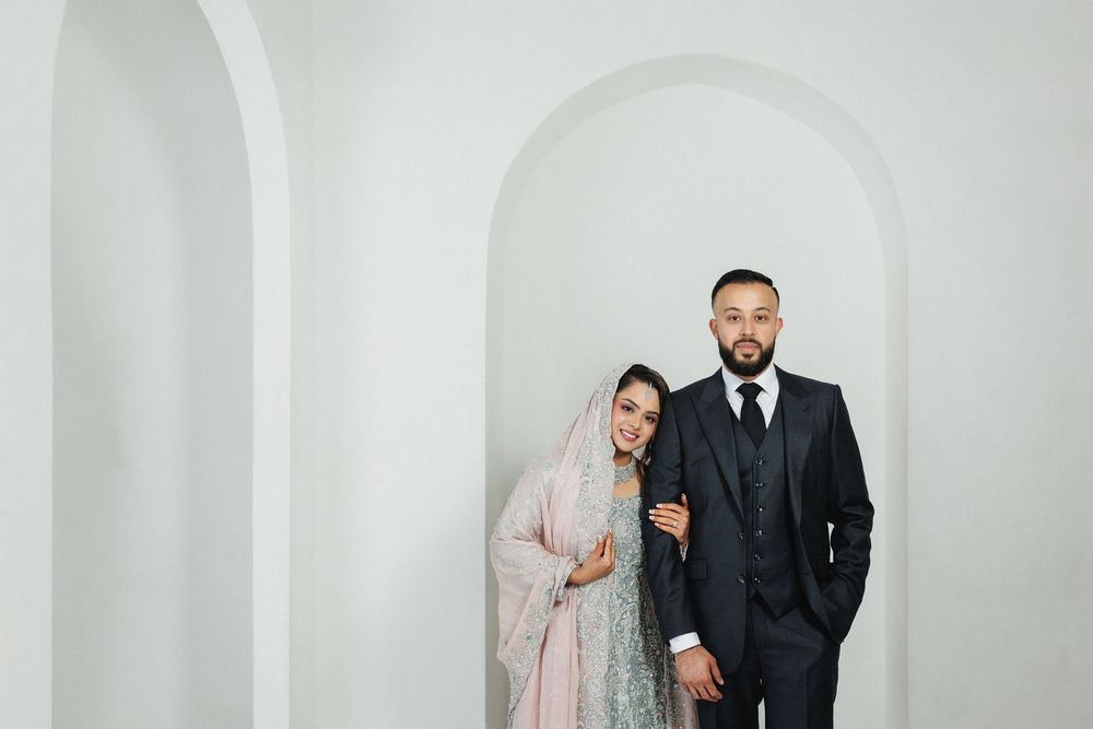 A couple poses together against white arches in traditional wedding attire.