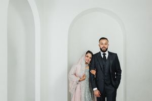 A couple poses together against white arches in traditional wedding attire.