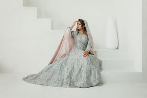 A bride in an elegant silver embellished lehenga poses gracefully against a white minimalist backdrop.