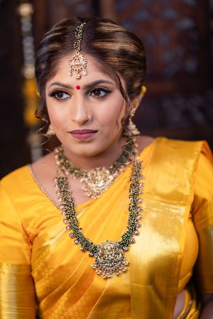 A woman in traditional Indian attire wearing a bright yellow saree and ornate jewelry poses for bridal portraits.