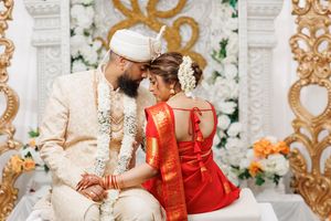 A couple in traditional red and gold wedding attire embrace during their Indian wedding ceremony.