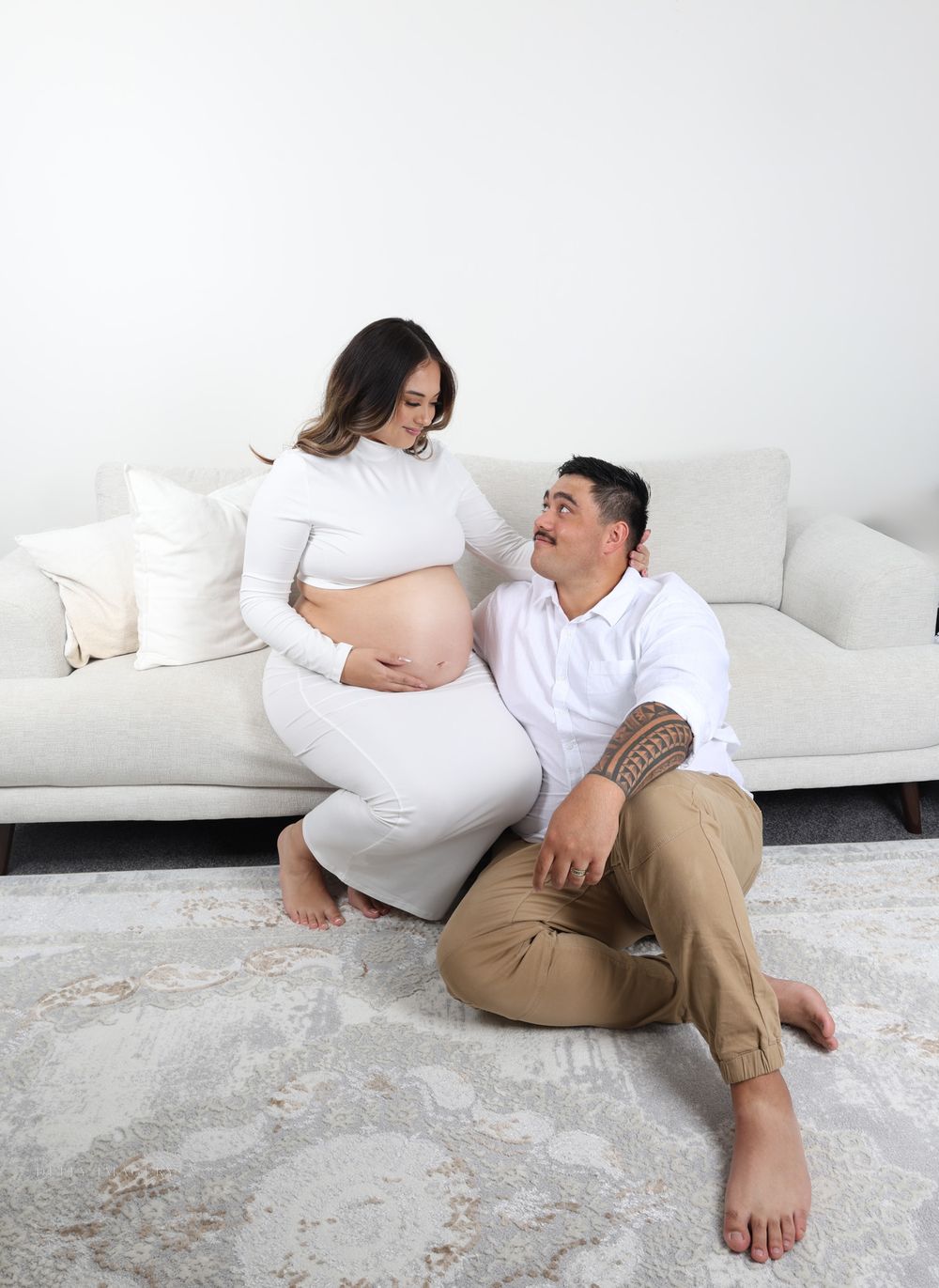 Casual maternity portrait of couple sitting together on white sofa.