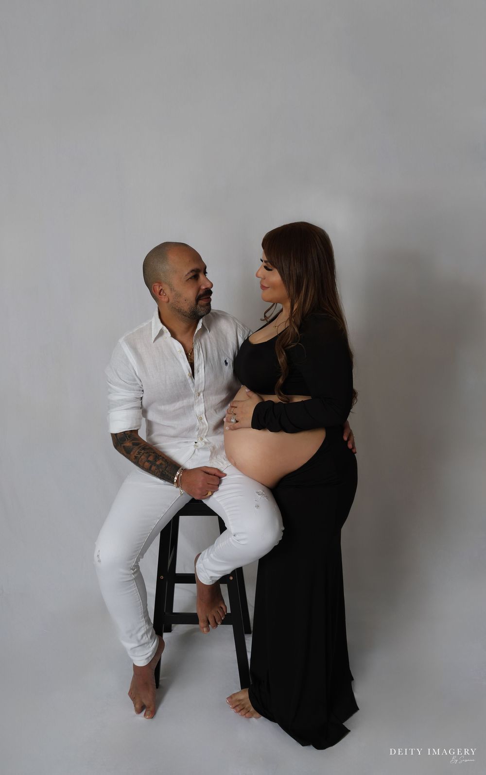 A couple in contrasting black and white outfits pose affectionately against a grey backdrop in a series of romantic photos.