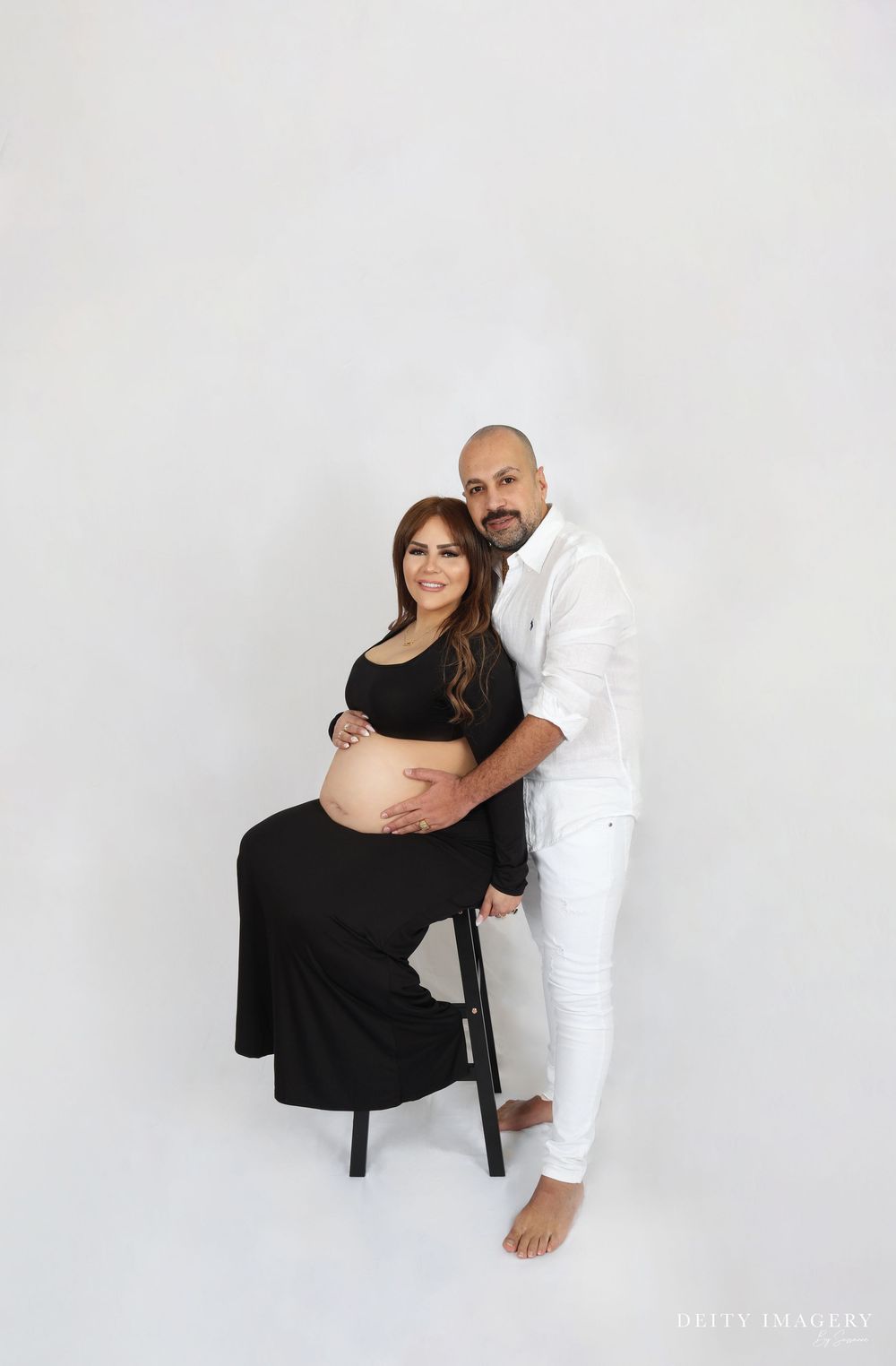 White and black clad figures pose together against a stark white background in artistic maternity photo series.