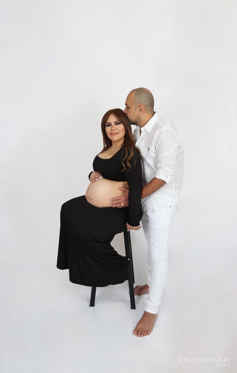 A couple in black and white attire embrace warmly against a plain white background during a professional photo shoot.