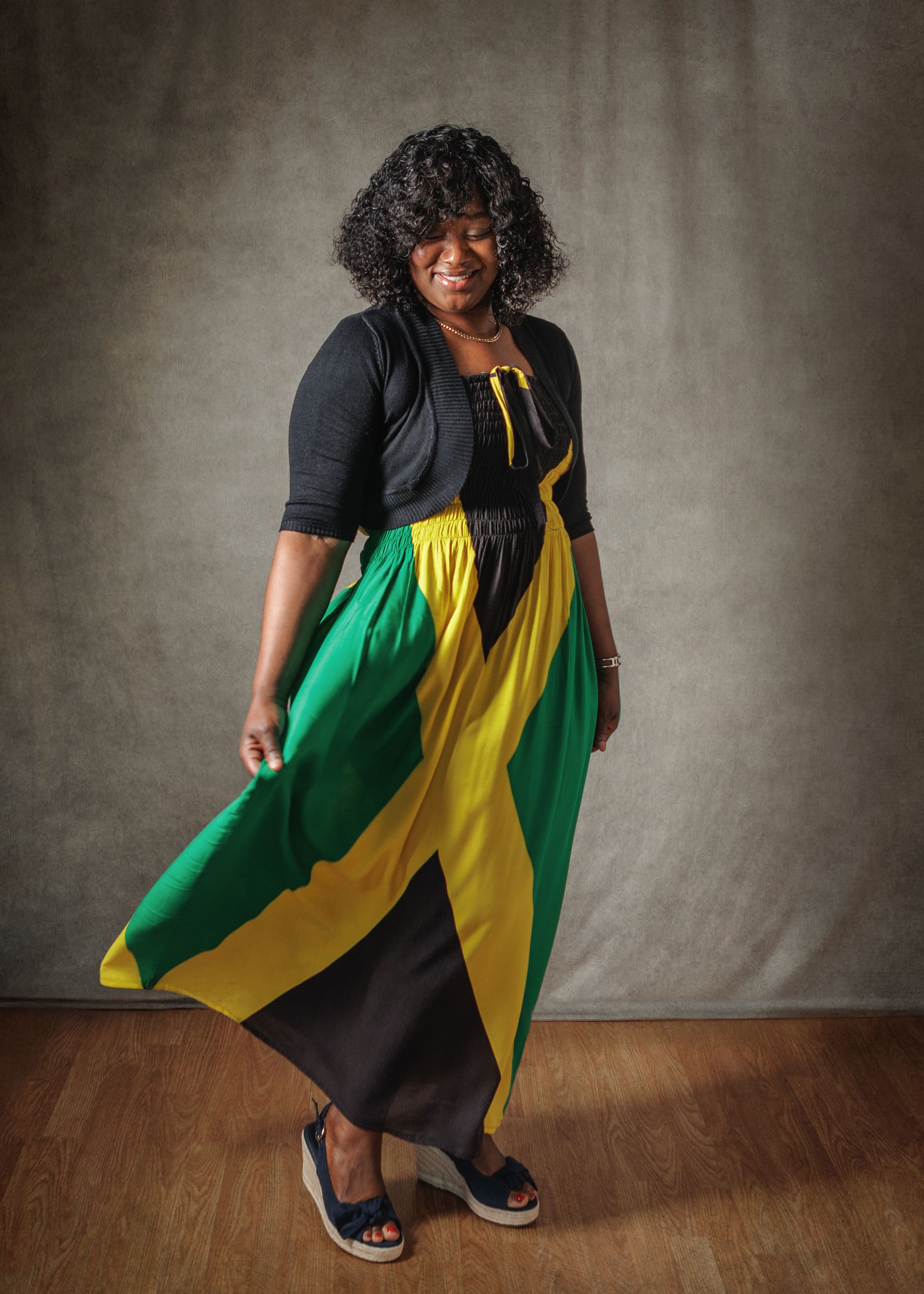 A person wearing a colorful dress in green, yellow and black twirls on a wooden floor against a gray backdrop.