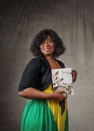 A person in a black cardigan and colorful yellow and green dress holds a book titled 'Pray' against a gray background.