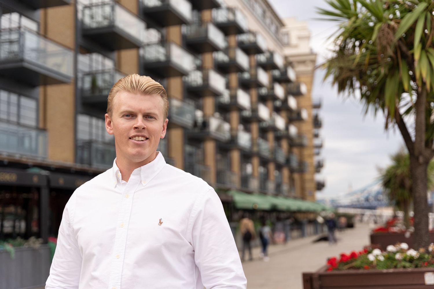 London business owner photography session by the river Thames. He wears a white shirt and is stood in front of some luxury apartments.