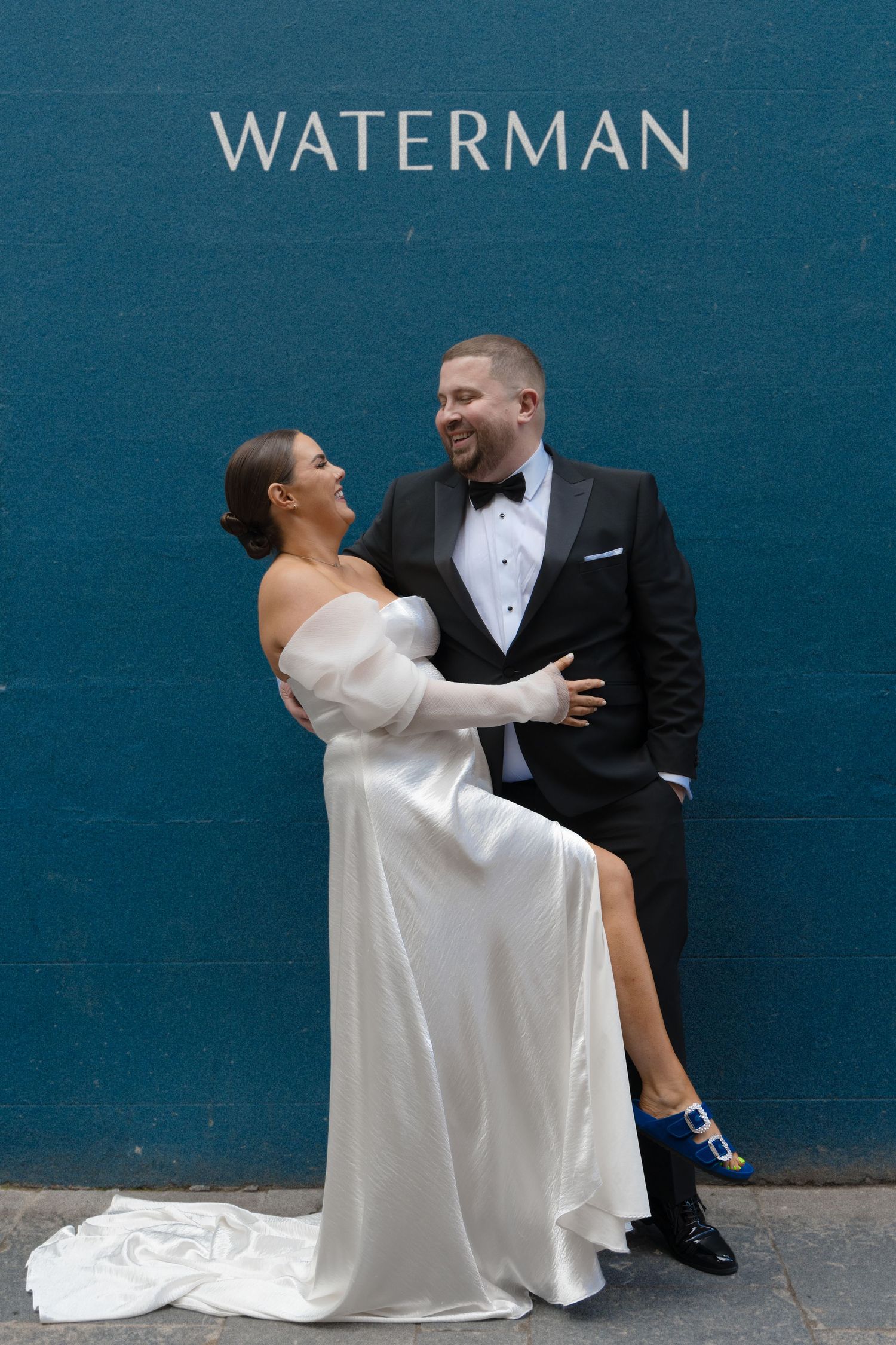 A couple shares a romantic kiss on their wedding day on an urban street with brick buildings in the background.