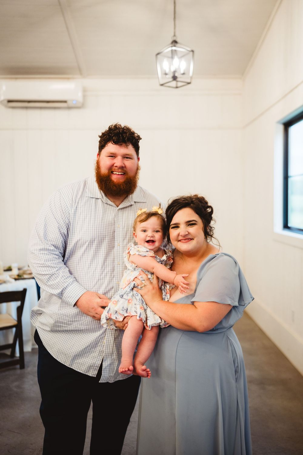 Three people pose together in a bright, minimalist indoor space with white walls and a pendant light fixture.