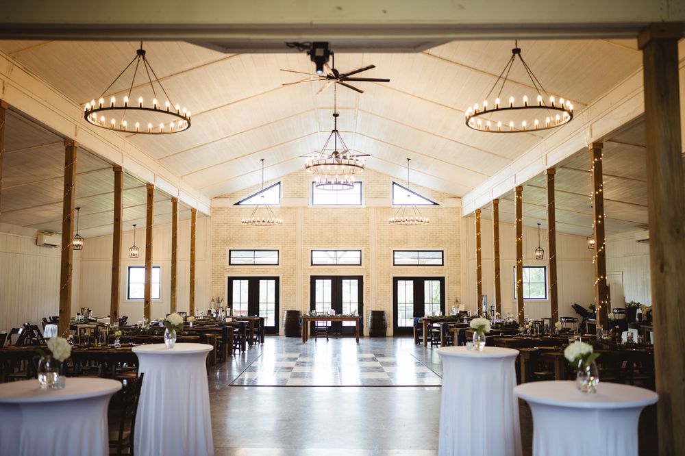A panoramic view of an elegant event venue interior with chandeliers, ceiling fans, and white draped decor.