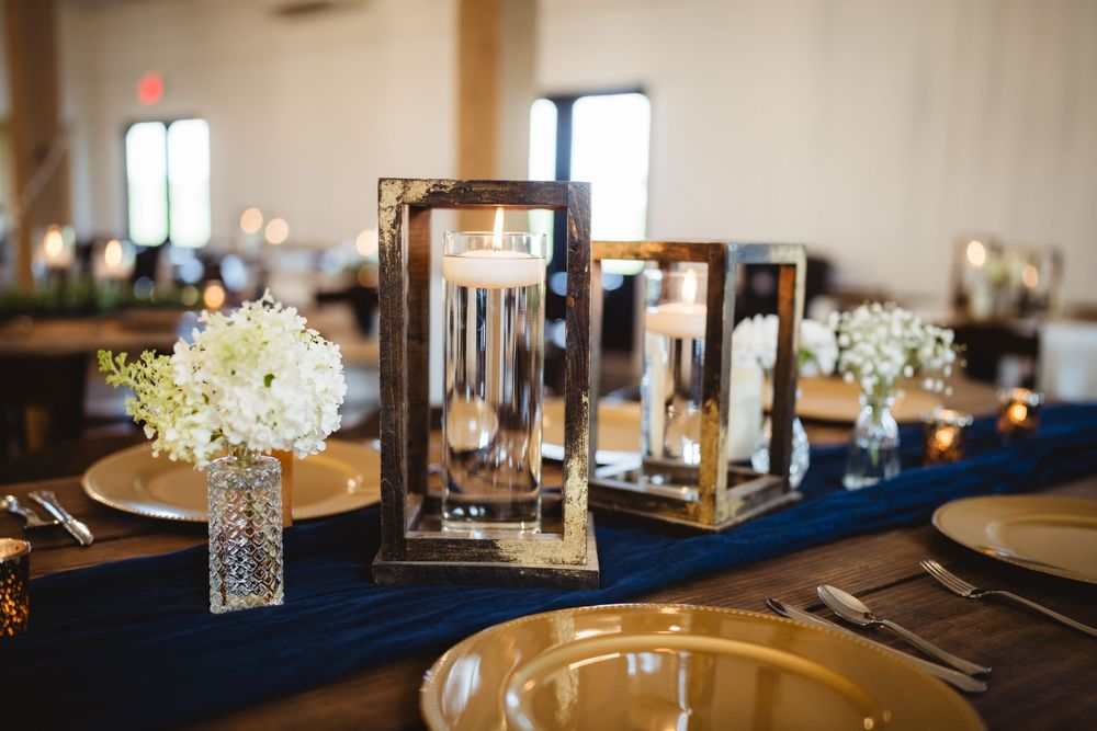Elegant wedding reception tables decorated with navy blue linens, white floral centerpieces, and glass candle holders.