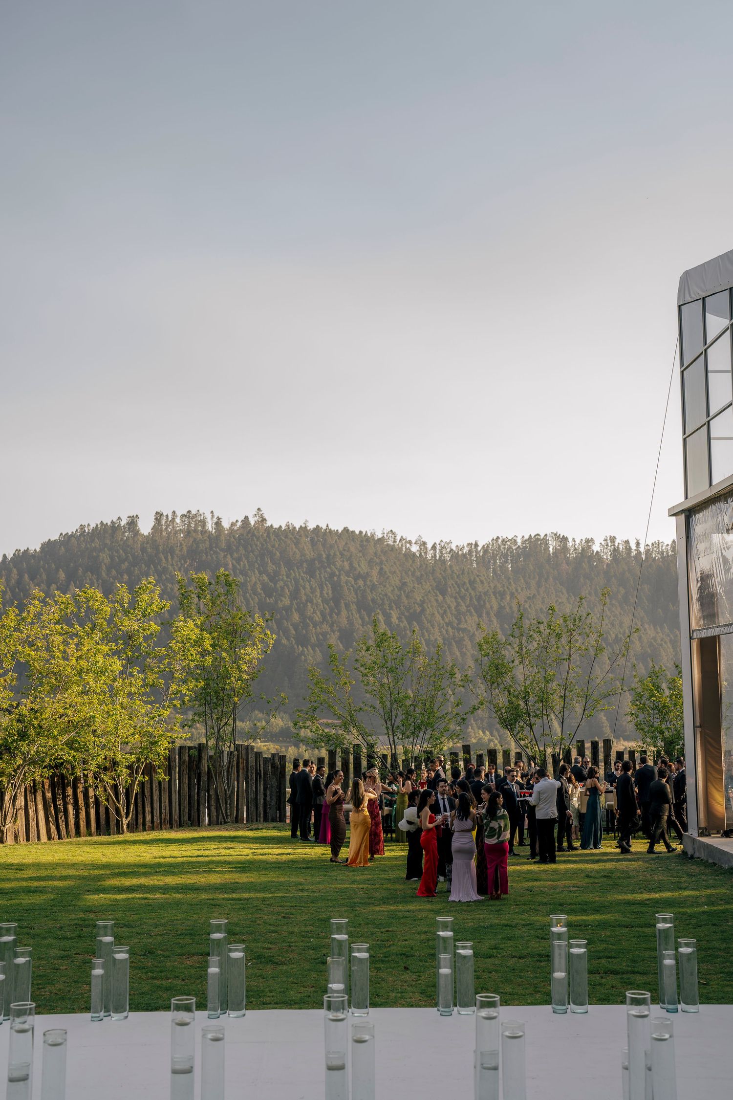 A panoramic view of people standing in front of tall metal pillars in a grassy field with trees in the background.