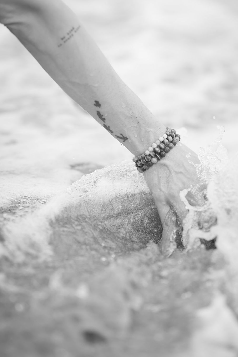 Black and white close-up shot of an arm with a bracelet on the wrist touching sandy beach surface.