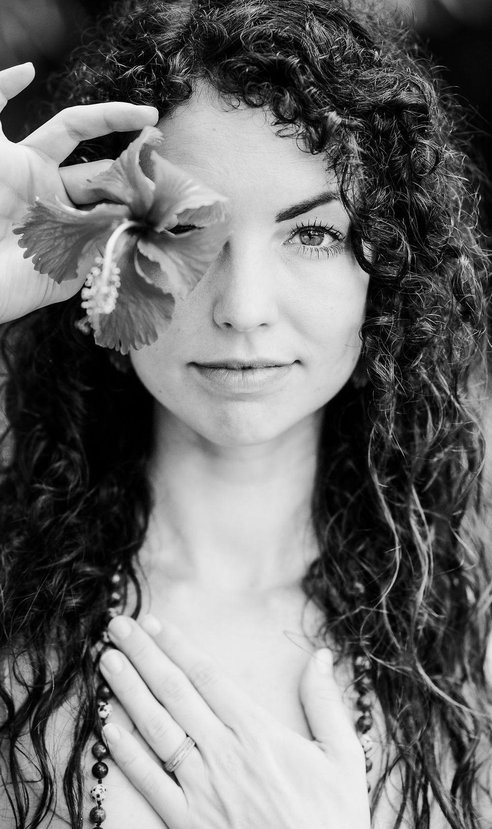 A black and white artistic portrait series showing someone with wild curly hair posing playfully with flowers.