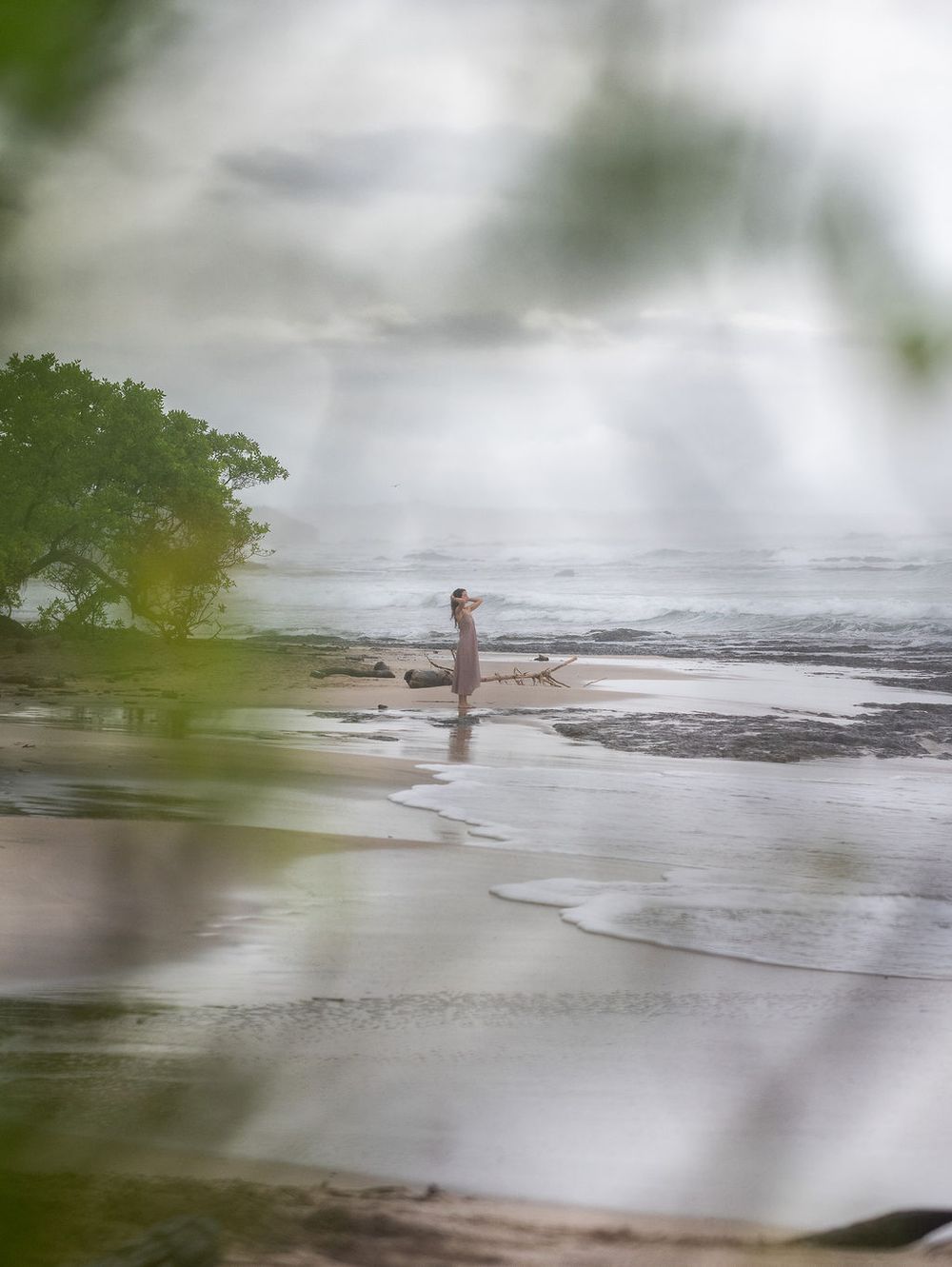 Person wading through a misty body of water surrounded by trees and blurry plant life in the foreground.