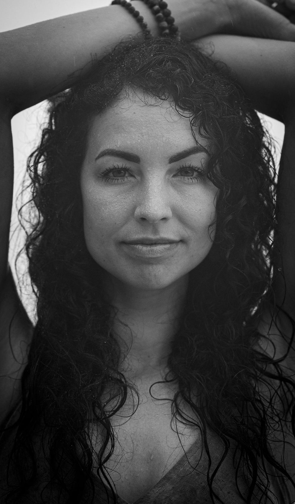Black and white portrait of a smiling young woman with long dark curly hair against a light background.