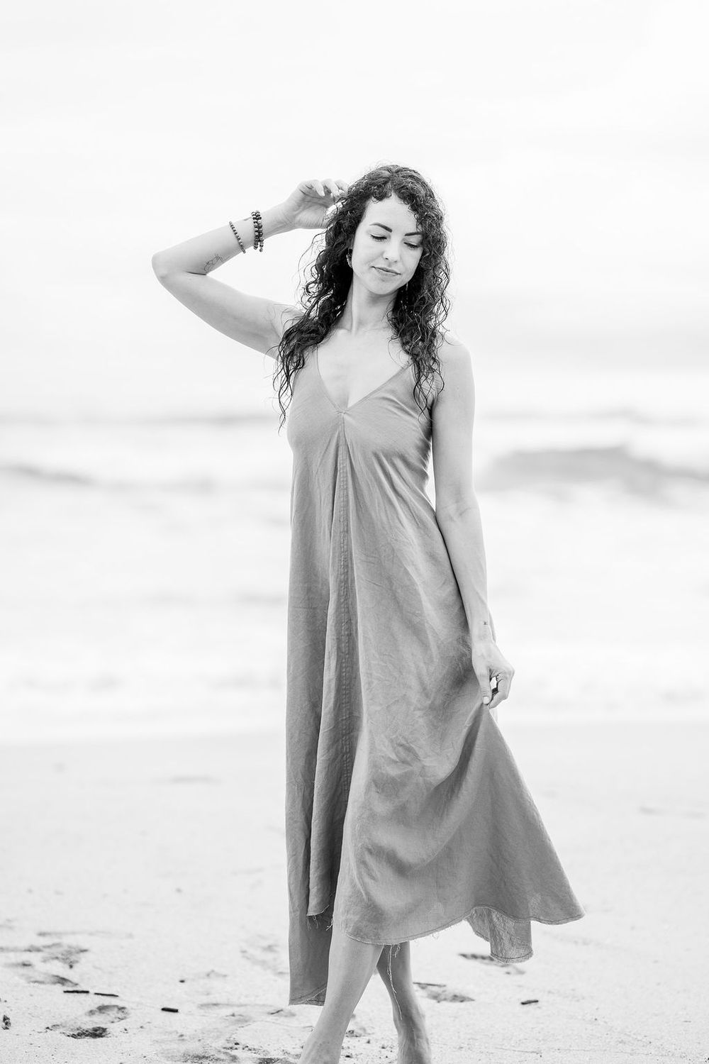 Black and white photo series of a young person in a flowing dress dancing expressively on the beach.