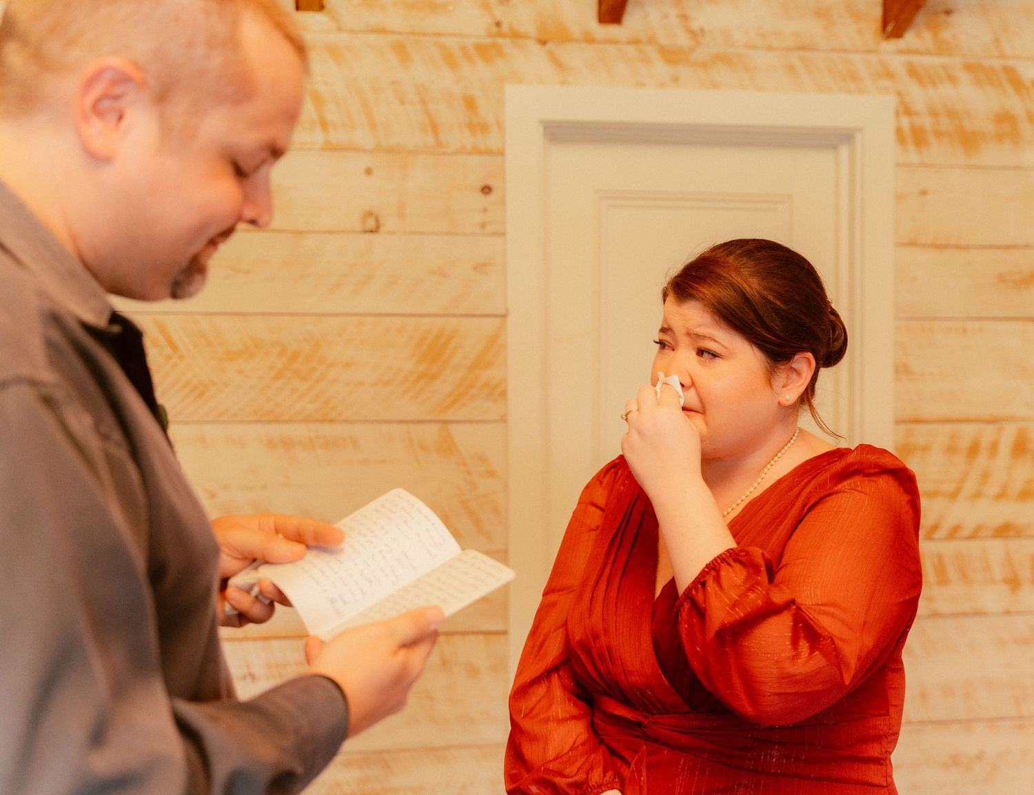 Two people share an emotional moment while looking at papers in a rustic interior setting.