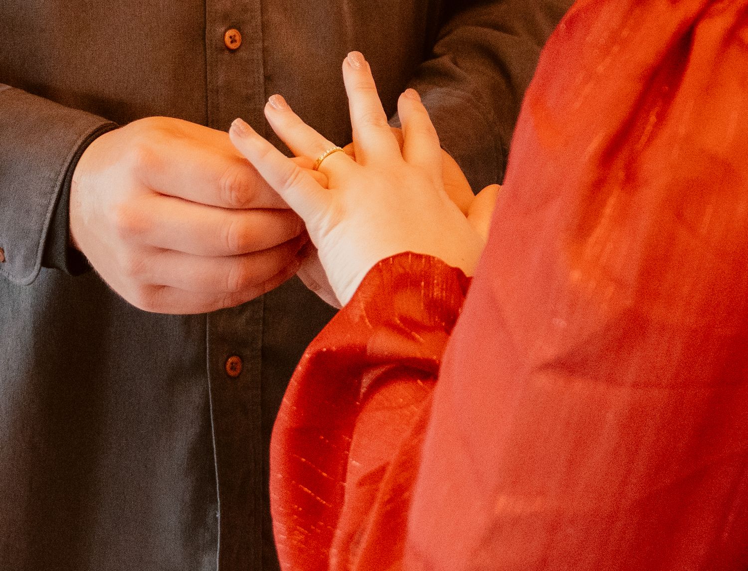 Close-up of hands exchanging rings during a wedding ceremony with a vibrant orange backdrop.