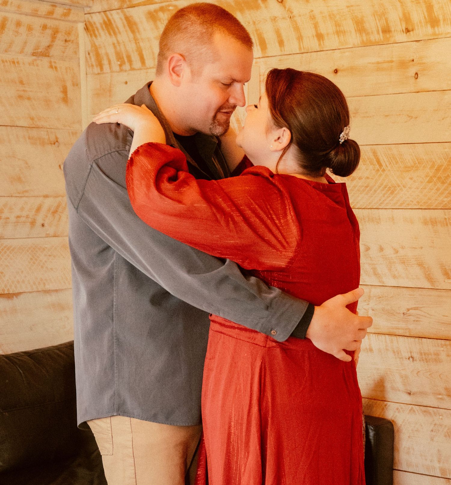 A romantic embrace between a couple in formal attire against a wooden wall backdrop.