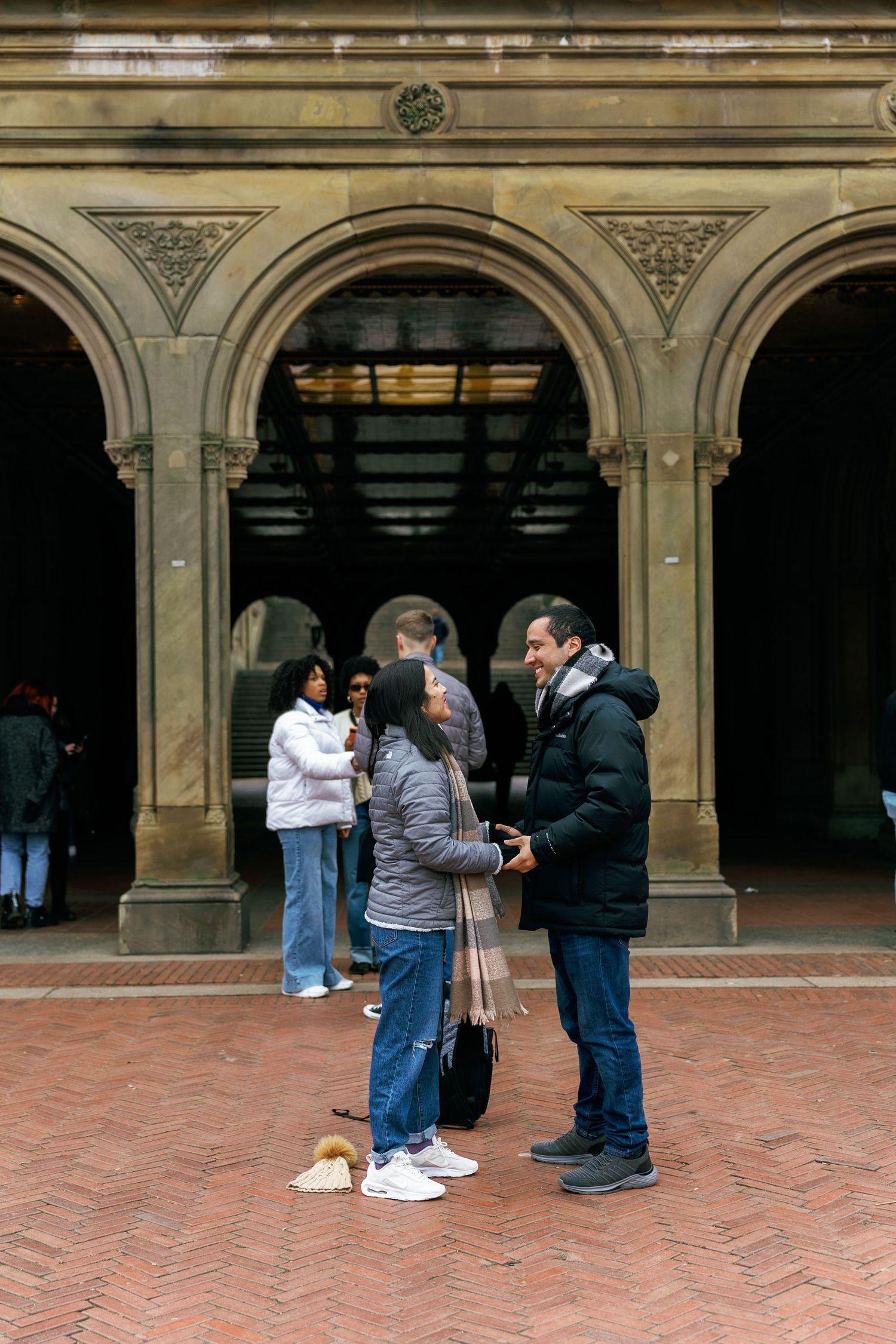 People gather and converse under ornate stone archways at Bethesda Terrace in Central Park.
