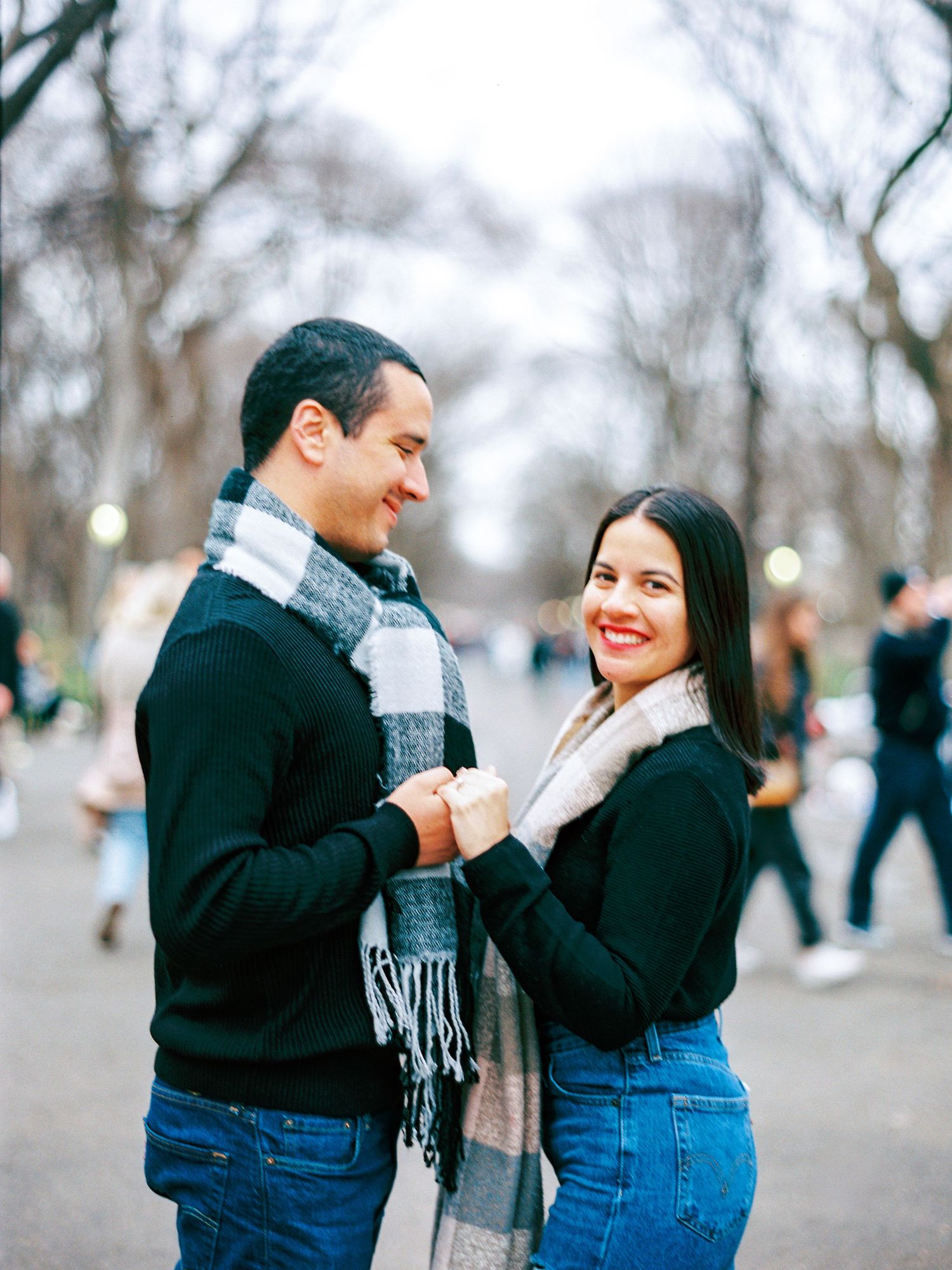 Two people share a joyful moment together outdoors in a park on a winter day wearing cozy sweaters and scarves.