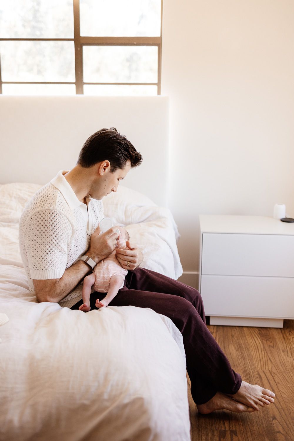 Bay Area Photographer Cindy Tucey captures image of a dad feeding his baby on a bed in a bright bedroom