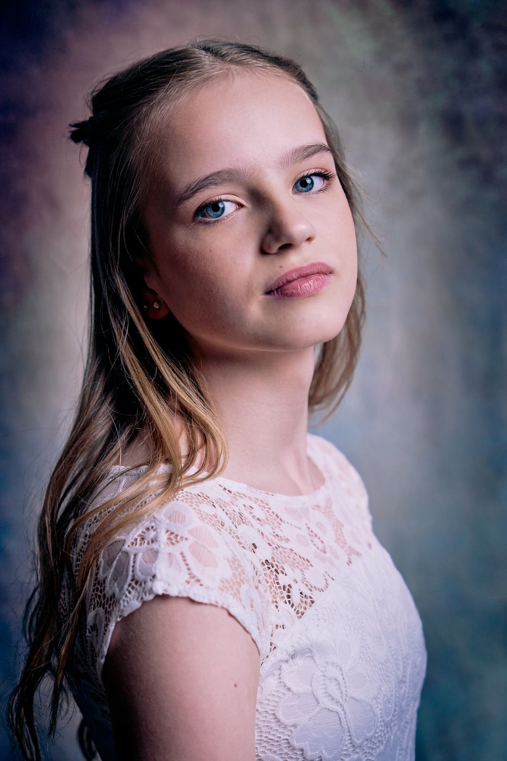 Portrait of young person wearing delicate white lace dress against misty studio backdrop with dramatic lighting.