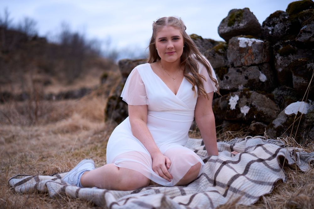 A person in a white dress sits on a blanket near a stone wall during golden hour.