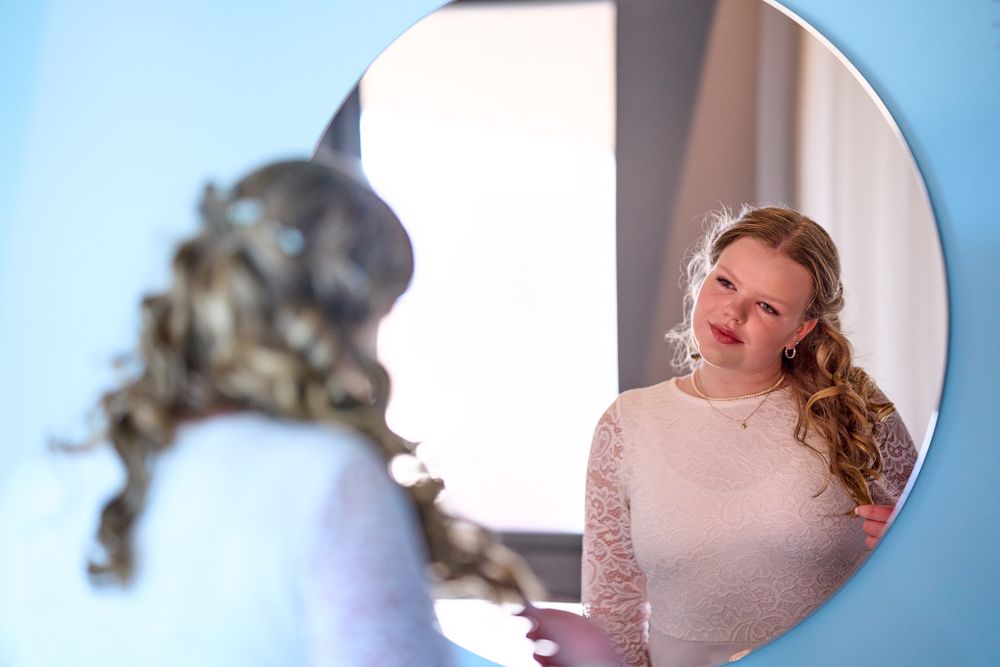 A reflection in an ornate mirror shows a person wearing a lace dress.